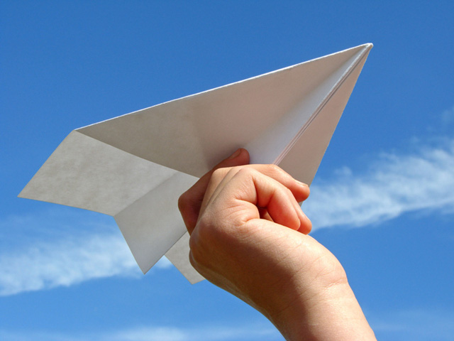 child hand with paper plane against blue sky
